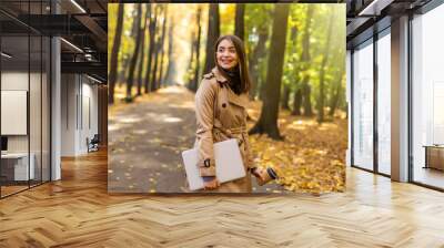 Young pretty woman walking laptop and coffee in autumn park. Wall mural